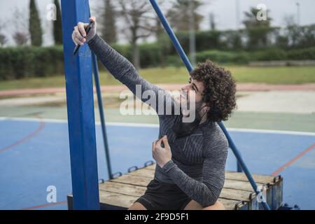 Shallow focus of a Caucasian curly-haired man in sportswear taking a selfie in a park Stock Photo