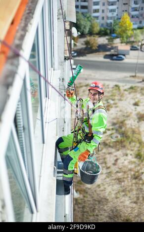 Cheerful industrial climber on building during winterization works, looking up at camera and smiling Stock Photo