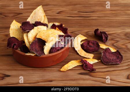 Mix of dried beetroot and pumpkin vegetable crisps lying in ceramic bowl on a wooden table. Closeup. Macro Stock Photo