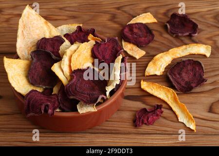 Mix of dried beetroot and pumpkin vegetable crisps lying in ceramic bowl on a wooden table. Top down view. Closeup. Macro Stock Photo