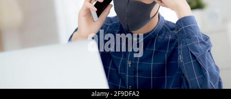 Young asian business man in face mask talking smartphone and work on laptop computer for protect covid-19, businessman quarantine work from home with Stock Photo