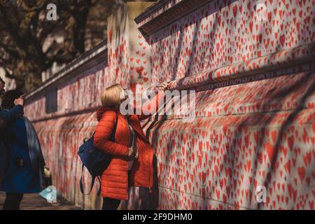 Westminster, London | UK - 2021.04.17: Lady writing names on The National COVID Memorial Wall painted with red hearts on beautiful sunny day Westminster, London | UK - 2021.04.17: Lady writing names on The National COVID Memorial Wall painted with red hearts on beautiful sunny day