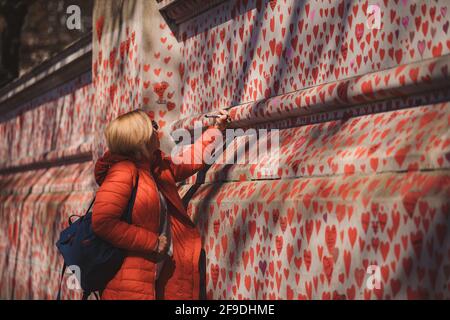 Westminster, London | UK -  2021.04.17: Lady writing names on The National COVID Memorial Wall painted with red hearts on beautiful sunny day