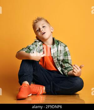 Romantic kid boy teenager in casual clothing and sneakers sits on floor playing an imaginary guitar and sings Stock Photo