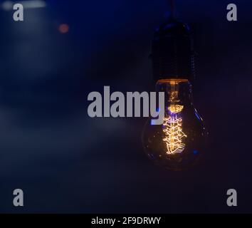 Close up of a glowing light bulb hanging in the dark copy space. Stock Photo