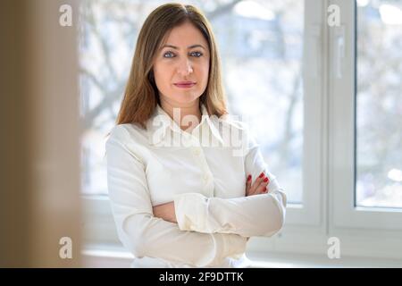 Confident astute middle-aged businesswoman standing with folded arms looking calmly at the camera with a penetrating stare in close up Stock Photo