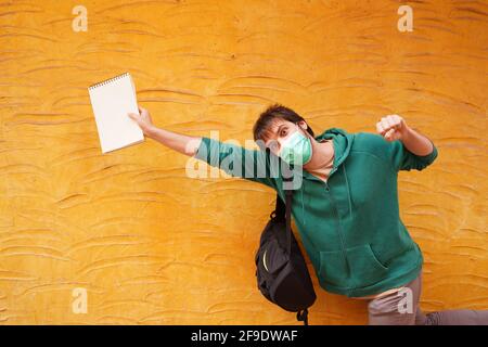A closeup shot of a young Spanish man posing with a notebook and backpack on an orange wall background Stock Photo
