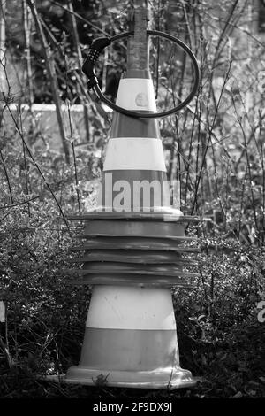 stacked and connected barrier pylons on a metal rod secured with a combination lock in black an white monochrome streetart Stock Photo