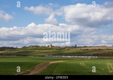 Green fields and blue sky, with a C2C train passing by Hadleigh Castle in the distance, from Hadleigh Ray, Essex, England. Stock Photo