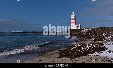 Beautiful view of white and red colored old lighthouse Garður on the coast of Suðurnesjabær on Reykjanes peninsula, Iceland with beach and snow. Stock Photo