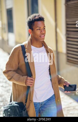 Young black man walking down the street carrying a briefcase and a smartphone. Stock Photo