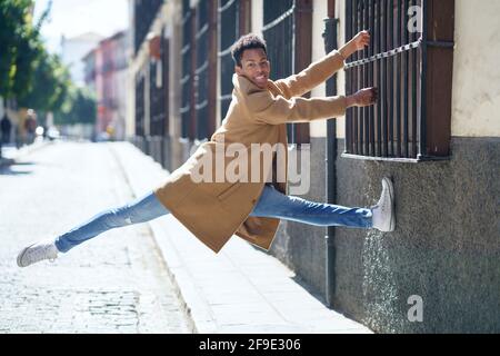 Young Cuban man jumping holding on to a window grille in the street. Stock Photo