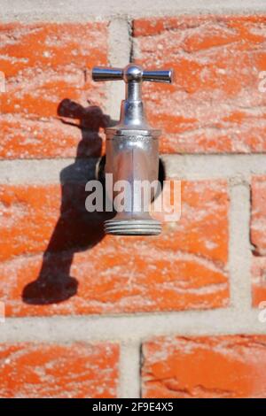 Silver colored metal faucet in sunlight on a brick house wall Stock Photo