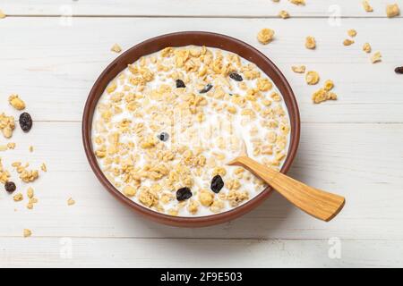Healthy breakfast. Muesli with dried grapes is poured with milk in a clay bowl on a white wooden table. Muesli is scattered on the table. Space for te Stock Photo