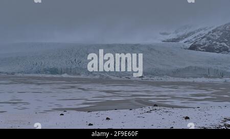 Front view of glacial lake Fjallsárlón in south Iceland with Fjallsjökull glacier, part of the Vatnajökull ice cap, and rugged mountains in clouds. Stock Photo