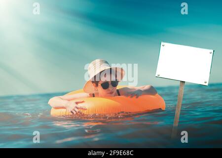 A young woman in a black swimsuit and hat, bathing with a circle in the sea. On the face of the emotions of fear and panic. Concept of swimming traini Stock Photo