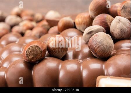 Chocolate bars with nuts. Pile of chocolate pieces with hazelnuts on wooden background. Different sorts chocolate and hazelnuts. Heap of broken chocol Stock Photo