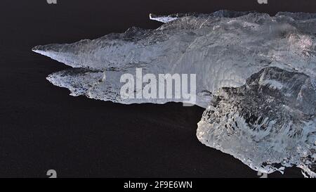 Closeup view of strange looking iceberg with beautiful ice surface shimmering in the evening sun in black sand of diamond beach in southern Iceland. Stock Photo