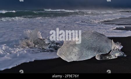 Wave breaking on small icebergs on diamond beach with black sand near Jökulsárlón glacier lagoon and ring road in southern Iceland at the ocean. Stock Photo