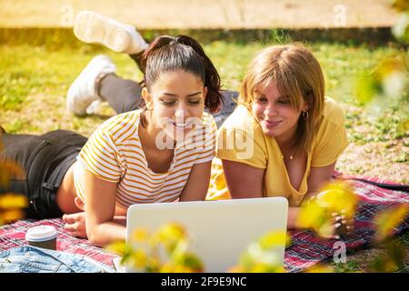 The Two Spanish women lying in the park and looking at a laptop on a sunny day Stock Photo