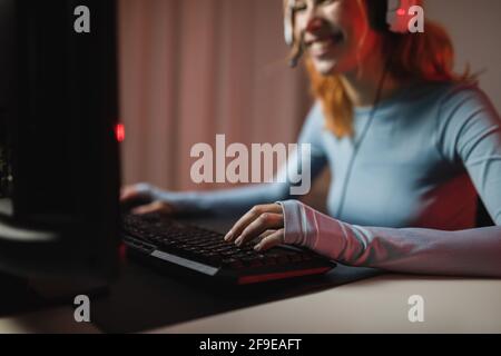 Side view of young slim barefoot female with brown wavy hair standing on balcony with raised arm and leaning on metal fence while practicing ballet in Stock Photo
