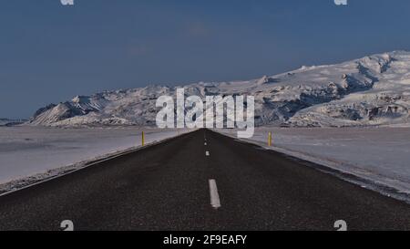 Beautiful diminishing perspective of empty, paved ring road (route 1) with markings on road trip in southern Iceland in winter season with snow. Stock Photo