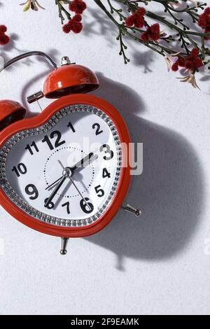 Top view of red alarm clock in shape of heart and bunch of fresh lavender flowers in vase arranged on white background in studio Stock Photo
