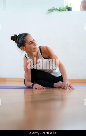 Ground level of middle aged female stretching legs and back while practicing yoga on mat and looking away in room Stock Photo