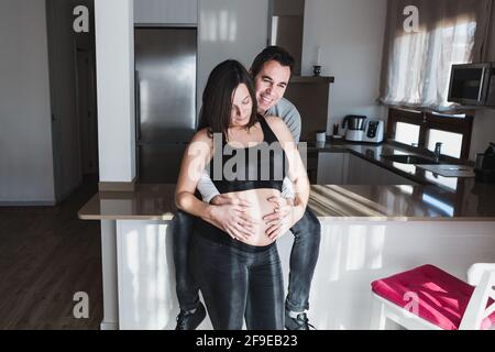 Delighted man touching tummy of pregnant Woman at home while enjoying weekend together Stock Photo