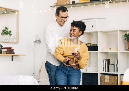 Delighted multiracial couple dancing in living room while spending time together at home Stock Photo
