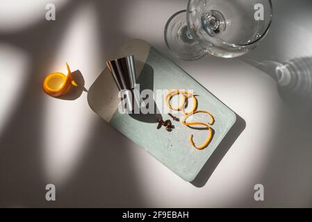 From above of glass near metal jigger with citrus fruit zest and dry condiments on table with shadows Stock Photo