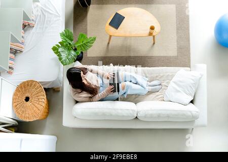 From above female browsing internet on portable computer with black screen while resting on sofa at home Stock Photo