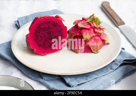 Bright tasty pitaya with juicy pulp and small seeds on ceramic plate near knife on table Stock Photo