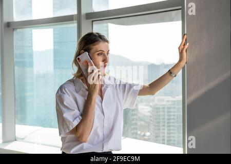 Young businessWoman standing in office with big windows having a phone call on the mobile phone Stock Photo