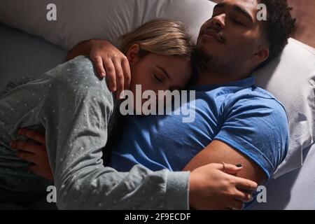 From above of serene multiethnic couple lying on bed and embracing while sleeping in cozy bedroom Stock Photo
