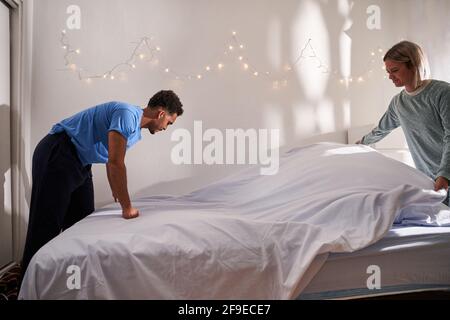 Side view of loving multiethnic couple in pajamas making bed together after awakening in morning Stock Photo
