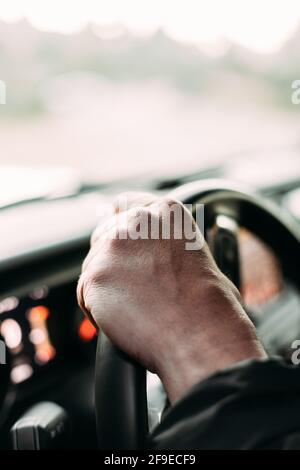 Crop view of anonymous man with her hand on a car steering wheel on blur background Stock Photo