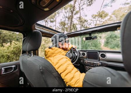 From behind inside view of a driver wearing a cap and sunglasses in an off-road car looking away Stock Photo