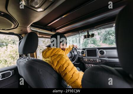 From behind inside view of a driver wearing a cap and sunglasses in an off-road car looking away Stock Photo