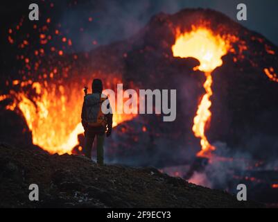 man explorer observing the magma sparks out of the volcano Fagradalsfjall in Iceland between clouds of smoke Stock Photo