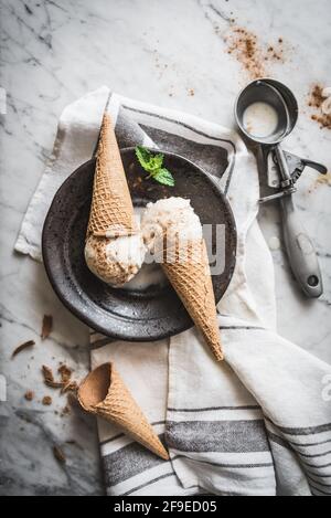From above of waffle cones with meringue milk gelato scoops and fresh mint leaves with cinnamon powder on top Stock Photo