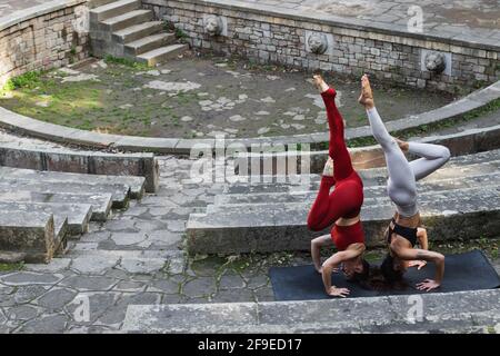 From above of fit females balancing in Salamba Sirsasana while practicing yoga together on mat on stone stairs Stock Photo