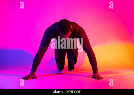 Full length concentrated fit African American male runner standing in crouch start position and looking down on colorful background in studio Stock Photo