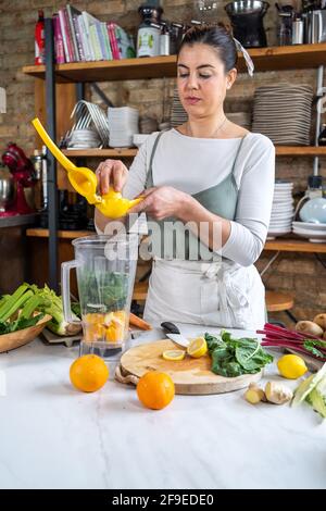 Content female squeezing lemon juice on chard leaves in blender bowl while preparing healthy drink in house kitchen Stock Photo