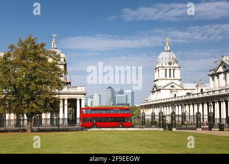 Red double decker bus in a central London scene. The Old Royal Naval College and National Maritime Museum in Greenwich Park. Canary Wharf skyline Stock Photo