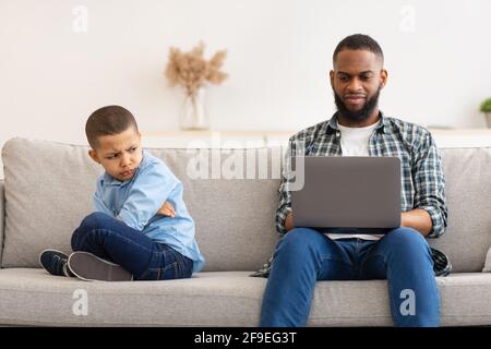 Reluctant Black Dad Ignoring Offended Son Using Laptop Indoors Stock Photo