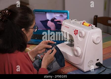 SANTA MARIA CAPUA VETERE, ITALY - Feb 08, 2021: Grandma taking a video tutorial on how to learn to use the sewing machine Stock Photo