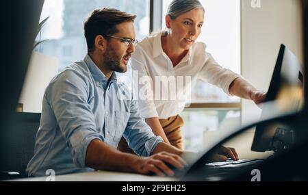 Manager pointing on computer screen and discussing work with colleague. Colleague helping man with improvements on report. Stock Photo