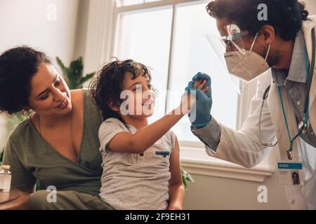 Doctor and child giving each other a high five after vaccination dose. Mother and son at home receiving vaccine during pandemic. Stock Photo