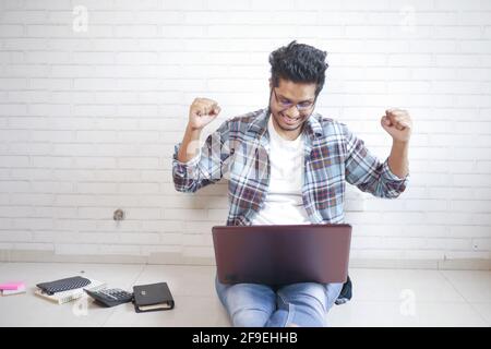 Work from home concept, happy young man sitting on floor working on laptop  Stock Photo